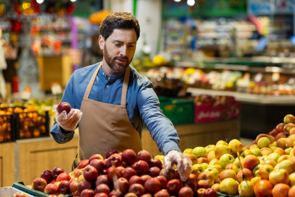 Commerçant en tablier disposant avec soin des fruits frais dans son magasin de quartier.